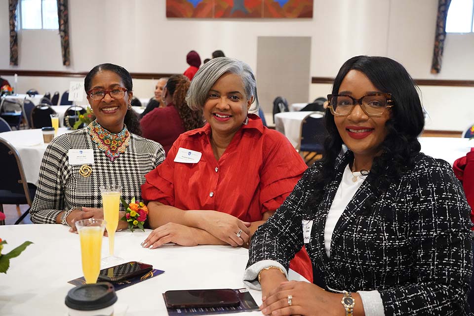 Three women pose for a photo while at a table in an event space.