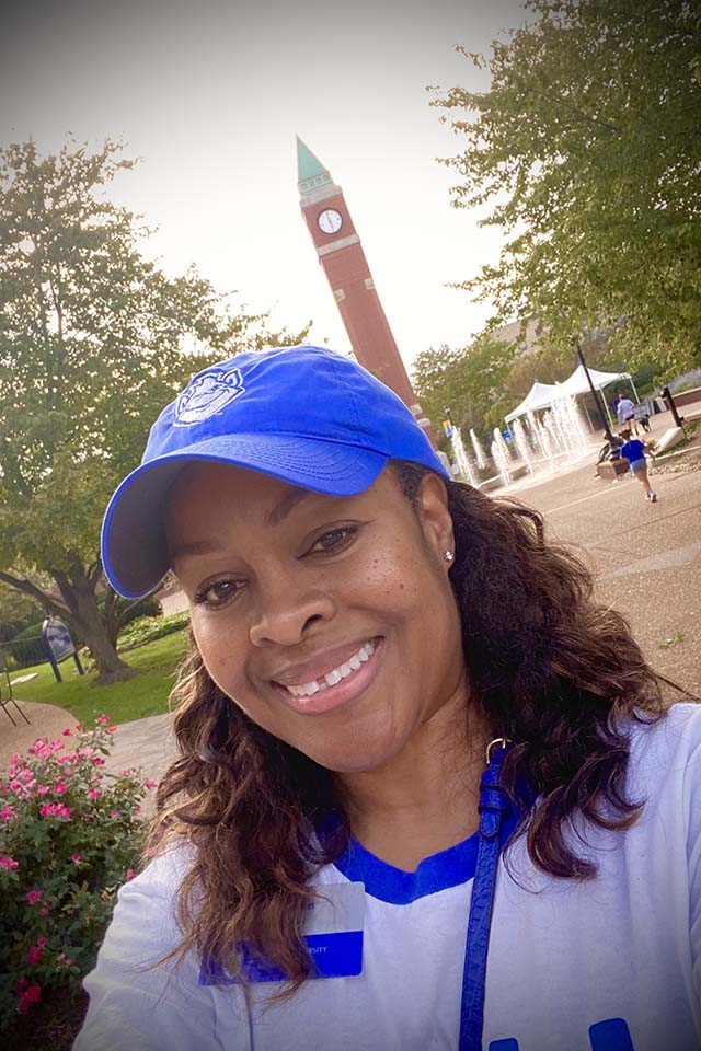 A woman poses for a selfie outside on campus with a clock tower behind her.