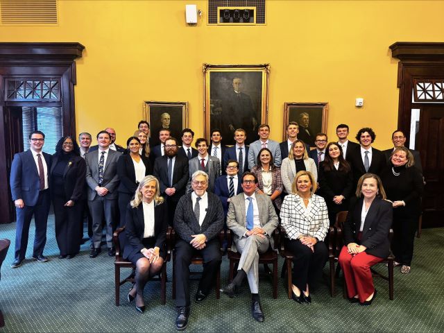 A large group of students and court members in professional dress pose for a photo in the courthouse.