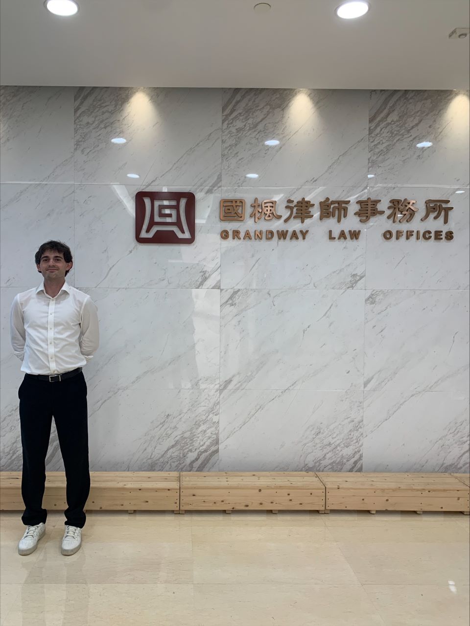 A student stands in a hallway next to a marble wall with a sign that reads Grandway Law Firm in English and Chinese characters Justin Fuller poses at the entrance of the firm in Shanghai were he worked over the summer
