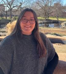 Woman with brown hair and glasses standing in front of stone building