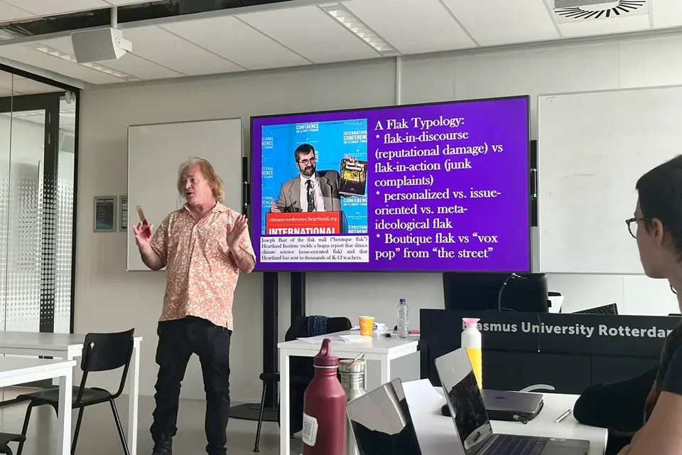 Brian Goss, Ph.D., presents at Erasmus University in Rotterdam Man speaks in front of large screen while facing the audience of students in a classroom. The screen has a slide explaining A Flak Typology.