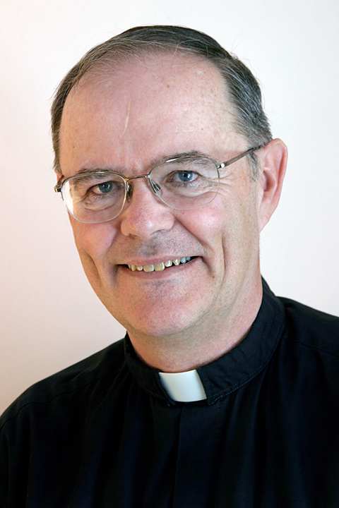 JJ Mueller An older white man wearing glasses and a Catholic priest's Roman collar