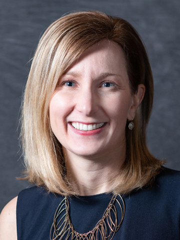 Laura Schrubb Laura Schrubb headshot, in black shirt with blonde hair and a grey backdrop.