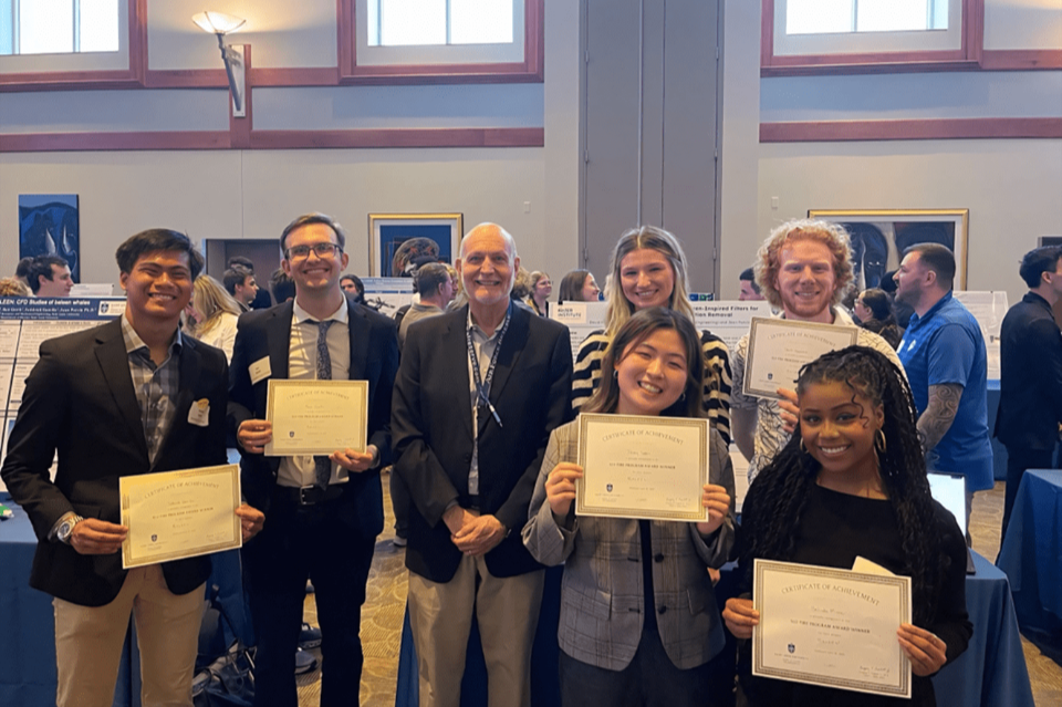 A group of students dressed professionally smile while holding up award certificates